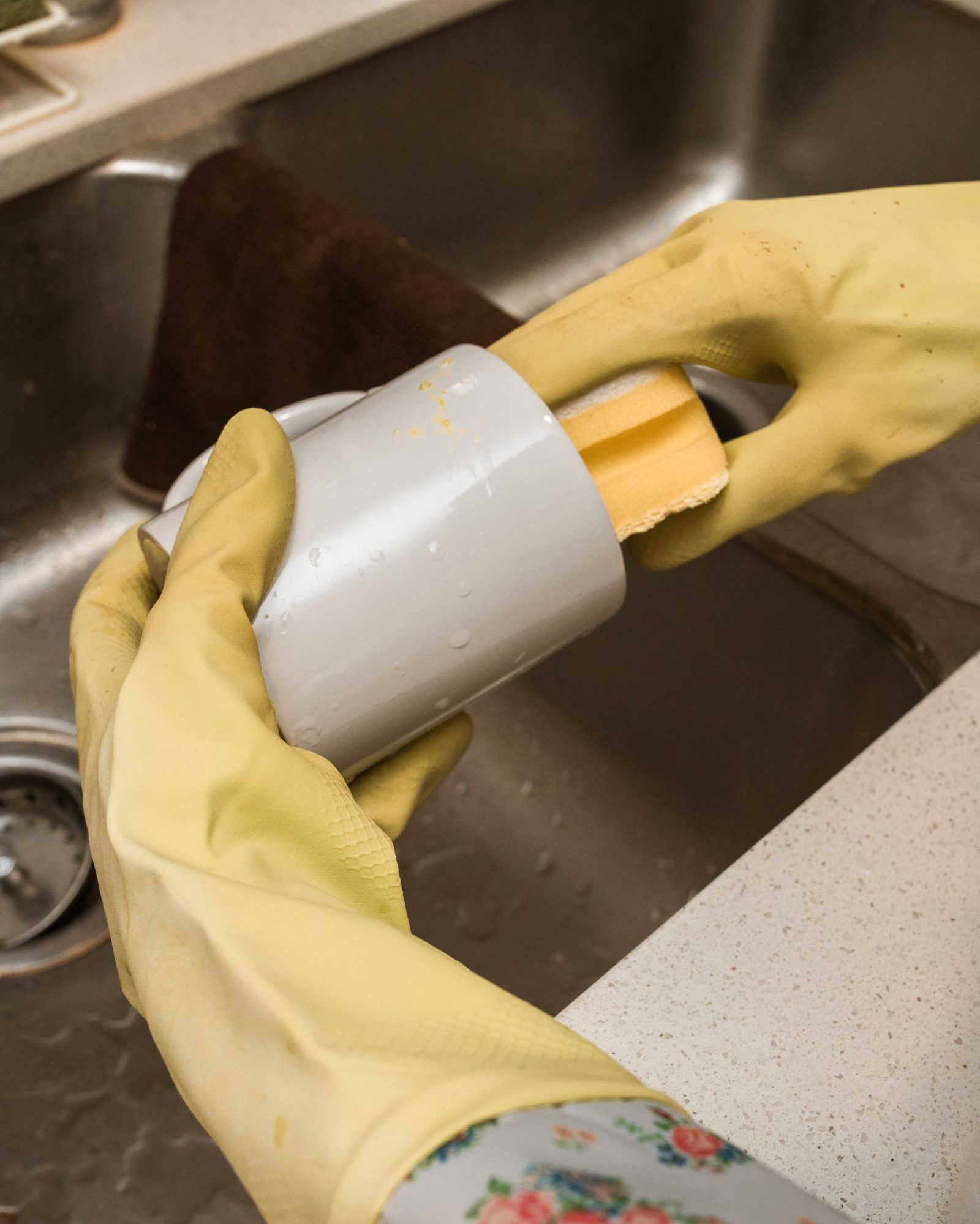 Évier de cuisine devant une fenêtre, gants jaunes posés sur le robinet, distributeur de savon et brosse à vaisselle